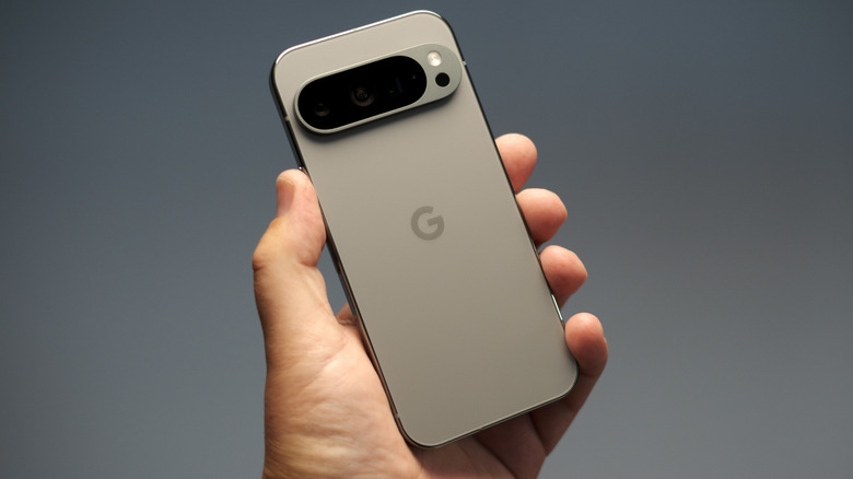 A gray Google Pixel device is held in an individual's left hand against a darkening gray backdrop