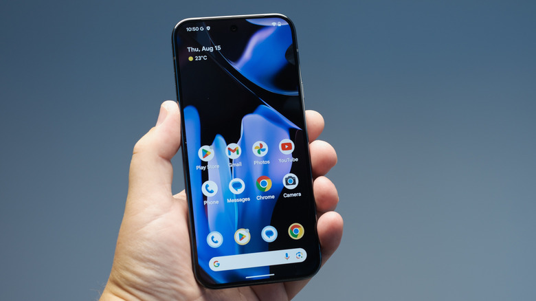 Pixel Phone held in hand showing home screen and three rows of apps