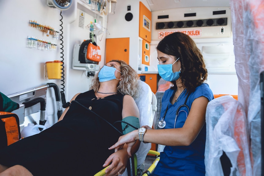 A paramedic takes the pulse of a female patient in the back of an ambulance