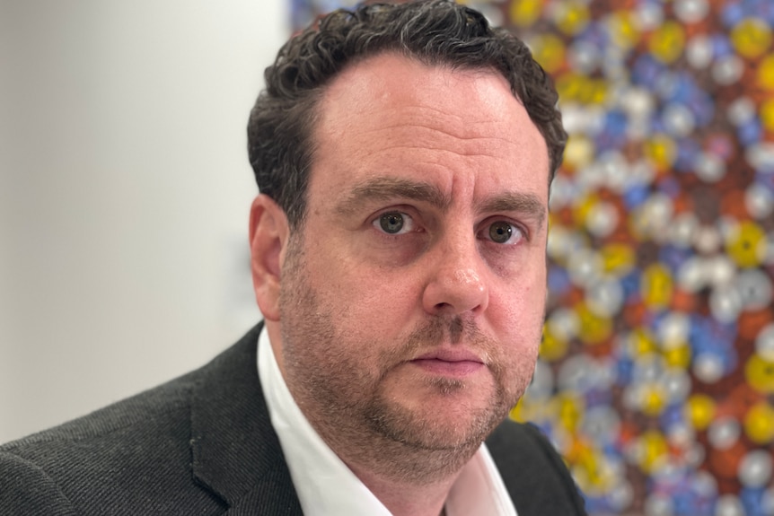 A man in front of a bright piece of artwork in his Marrickville office