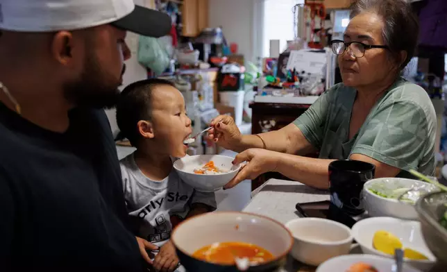 Lien Chang feeds her 2-year-old grandson Cairo Miu a bowl of rice next to his dad Jack Chang in her home on Monday, July 13, 2026, in San Francisco. (AP Photo/Juliana Yamada)