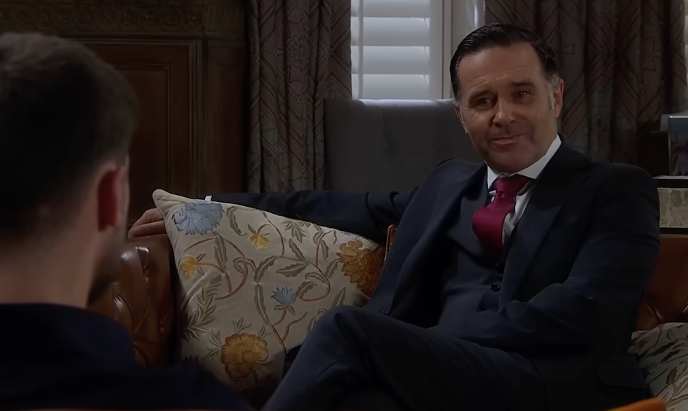 man in a suit sitting on a couch with patterned cushions in a dimly lit room. man in a suit sitting on a couch with patterned cushions in a dimly lit room.