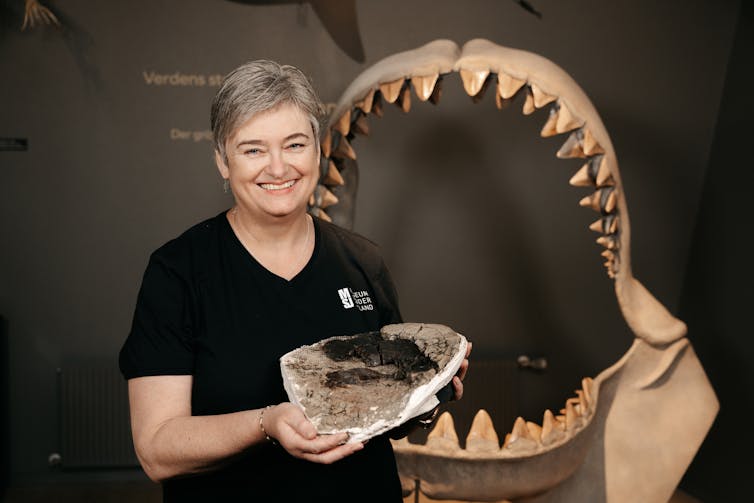 Woman holding giant piece of bone with reconstructed shark jaws in the background.