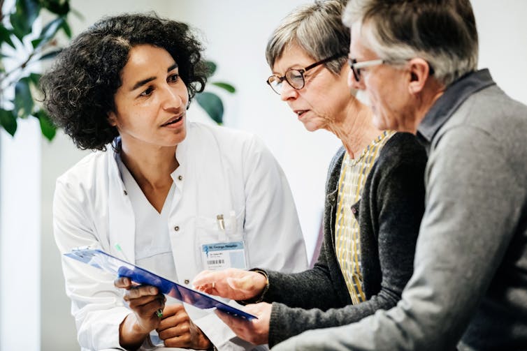 A doctor shows an older couple some test results on a tablet.
