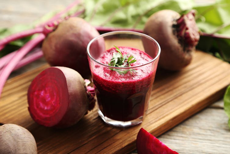 Beetroot juice on a wooden board, surrounded by beetroots.