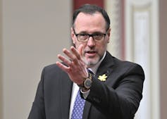 A man with thinning hair, a beard and glasses gestures as he speaks.