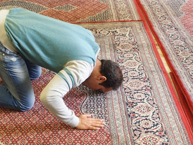 a man kneels on a carpet in prayer