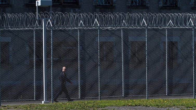 A correctional officer walks inside the fence of a penitentiary
