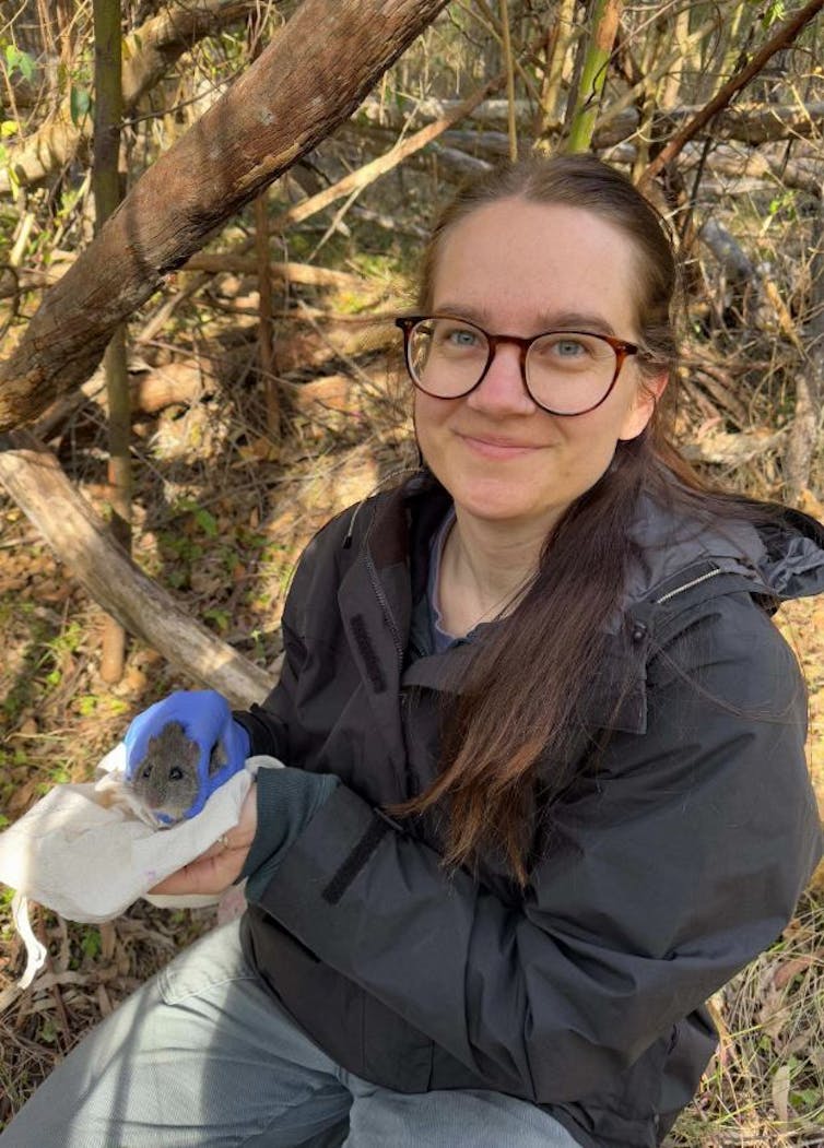 A young woman holds a small mouse in a calico bag, while conducting field research.