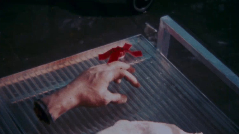 A living severed hand rests by a red-taped button in Flaming Ears