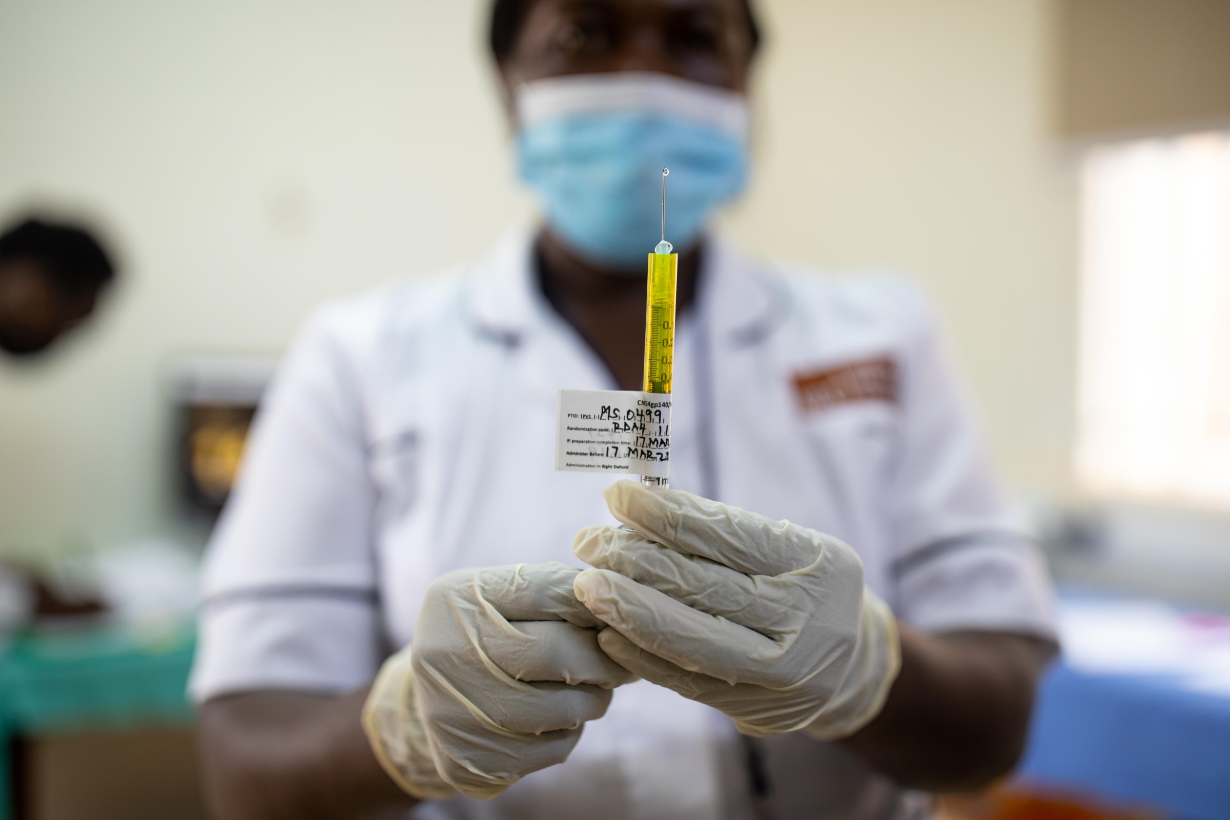 A nurse in a white shirt and latex gloves prepares an injectable needle.