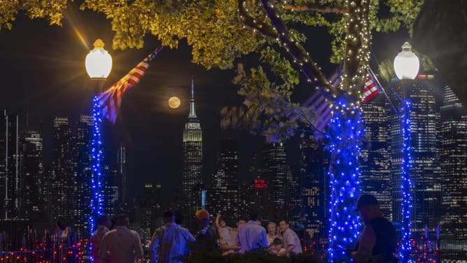 WEEHAWKEN, NJ - JUNE 29: The full Strawberry Moon rises behind the skyline of midtown Manhattan and the Empire State Building in New York City as people watch from a park on June 29, 2026, in Weehawken, New Jersey.