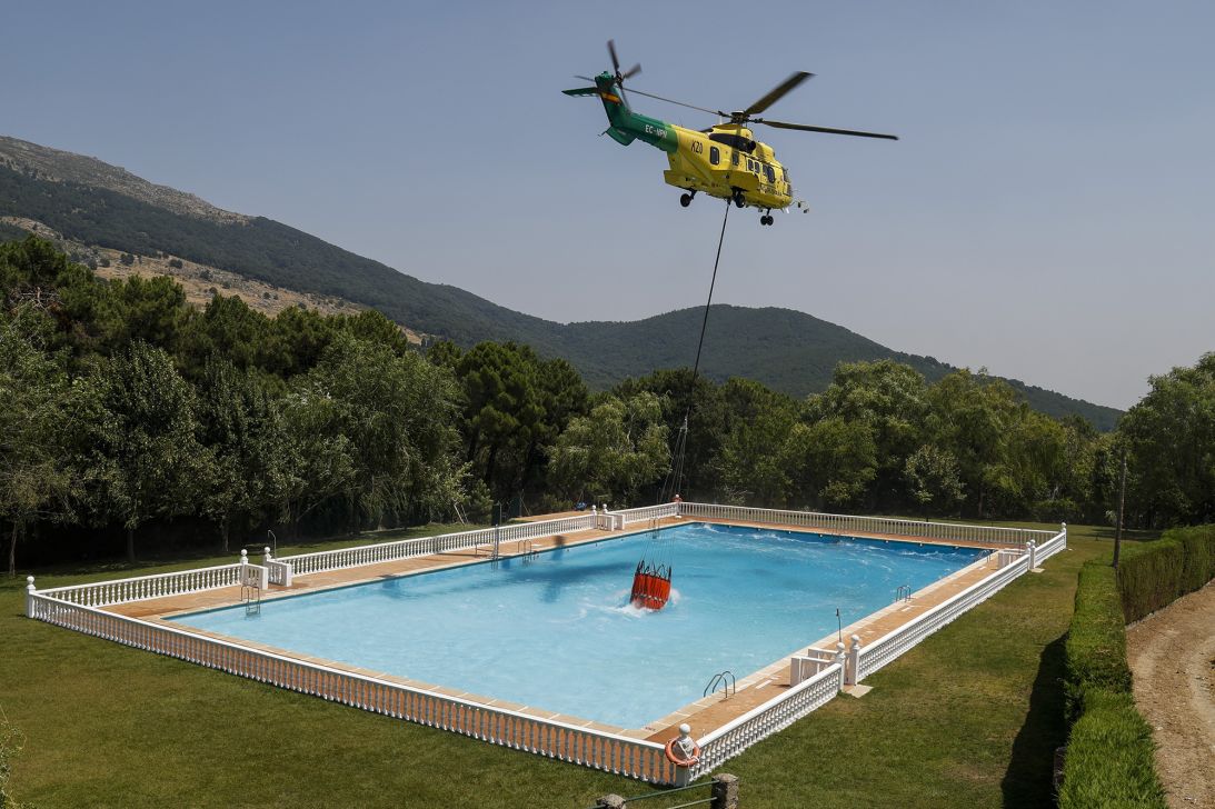 A helicopter collects water from a swimming pool to combat wildfires on July 28, 2026 in Casillas, in Ávila province, Spain.
