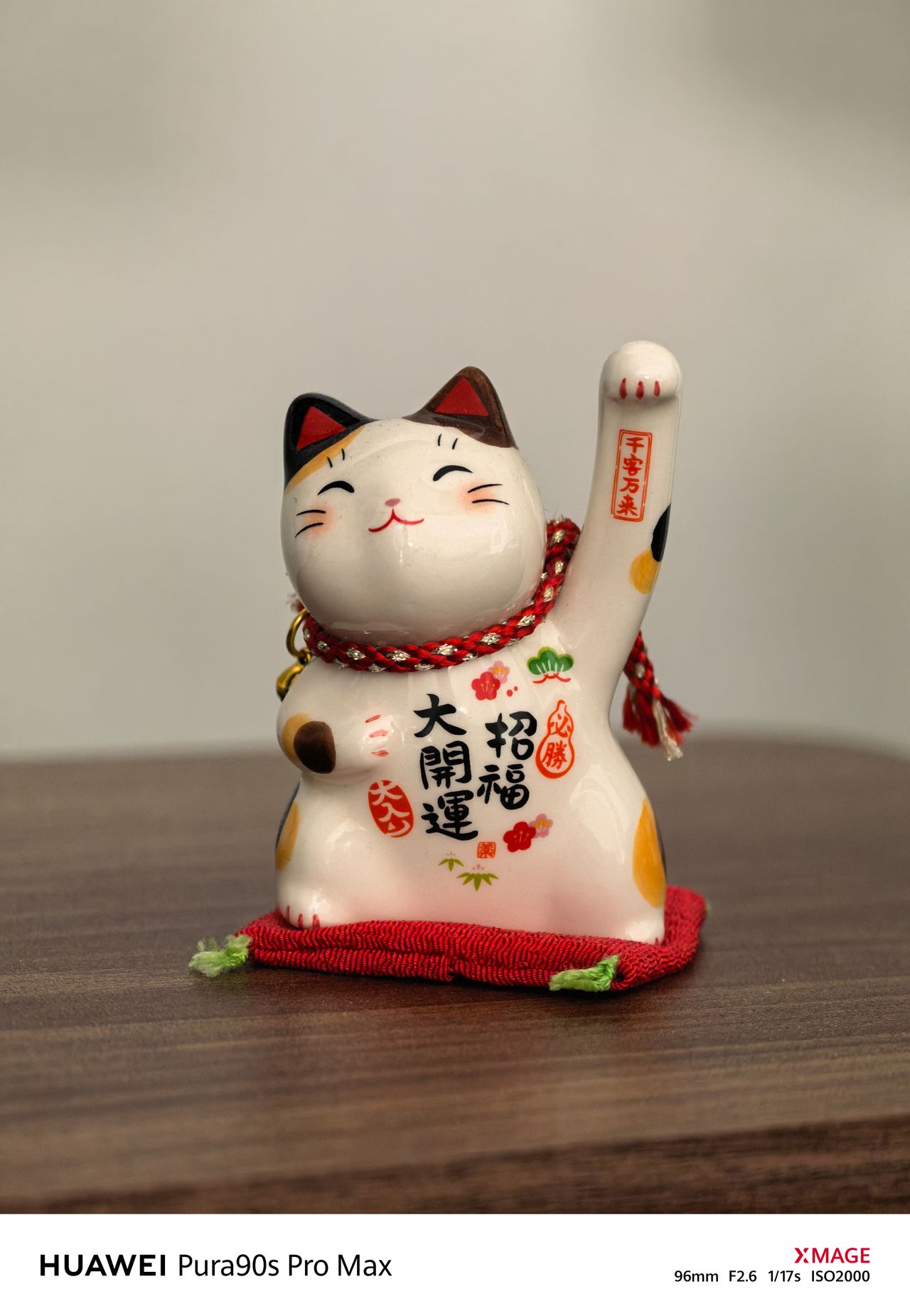 Ceramic Japanese lucky cat figurine with one raised paw, displayed on a wooden table.