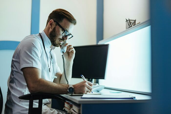A hospital employee working late at a desk, on the phone and taking notes, embodying hospital horror stories.