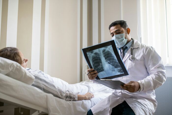 A hospital employee, a masked doctor, showing a patient an X-ray, illustrating hospital horror stories.