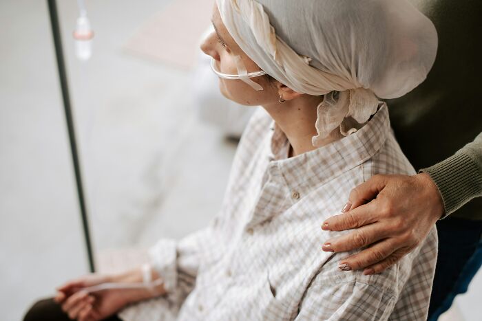 A hospital patient with an IV and headscarf, getting comfort from an employee, symbolizing hospital stories.