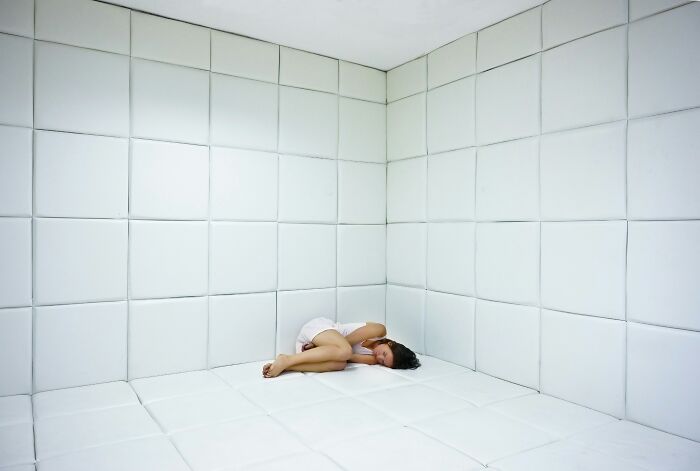 A person curled up on the floor of a padded room, symbolizing psychological hospital horror stories.