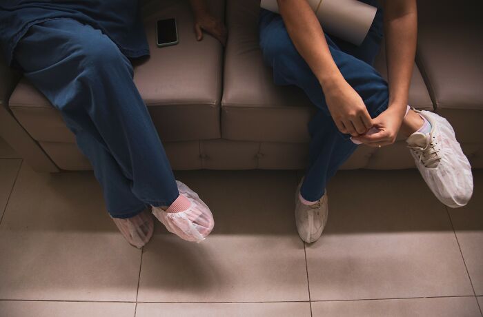 Hospital employees wearing scrubs and shoe covers, seated on a couch, representing hospital horror stories.