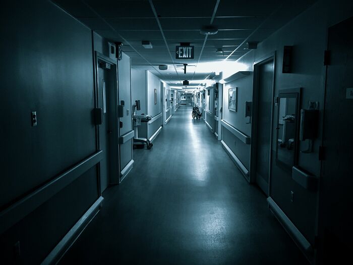 A long, dark hospital hallway with an exit sign, setting a scene for hospital horror stories.