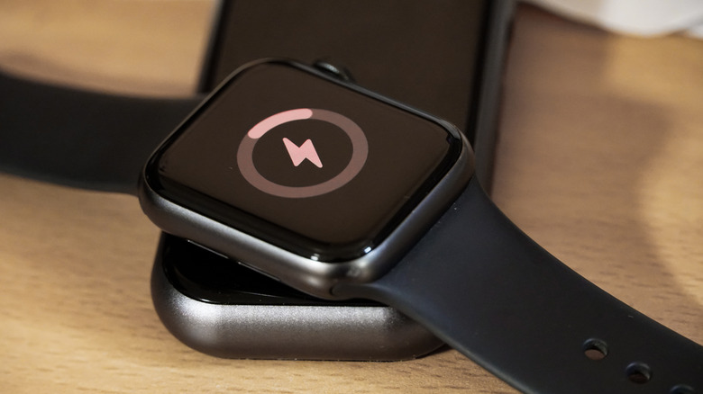 An Apple Watch atop a phone showing the charging symbol.