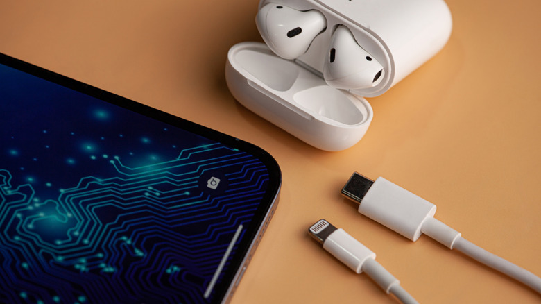 Apple AirPods in an open charging case, an iPhone, and USB-C to Lightning cable placed on an orange tabletop.