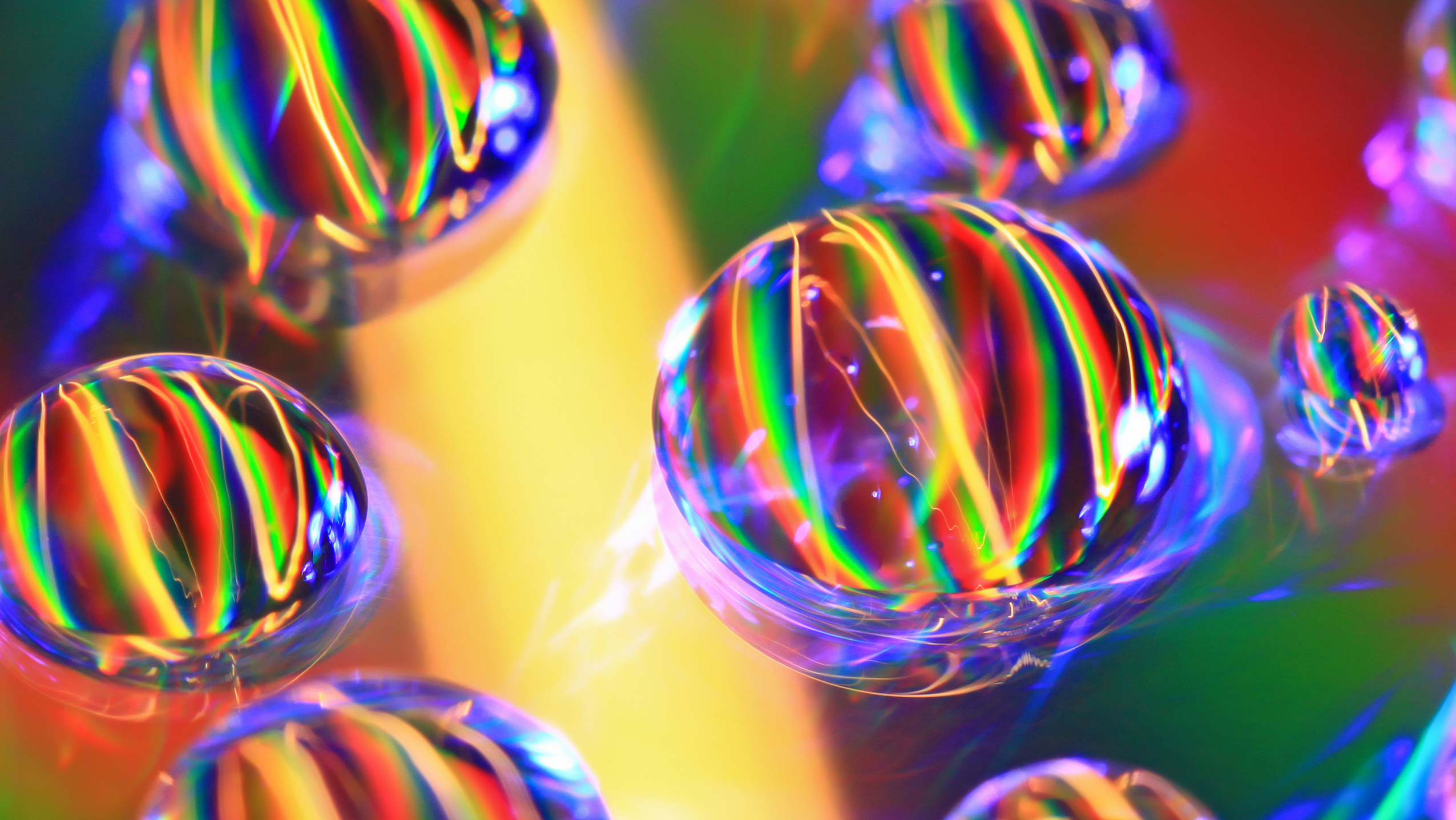 Close-up of water droplets on a colorful, iridescent surface, refracting light into vibrant rainbow patterns