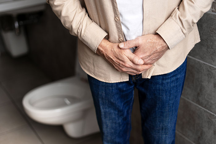 A person in jeans and a shirt holding their groin area in a bathroom, a medical symptom doctors wish people would not ignore.