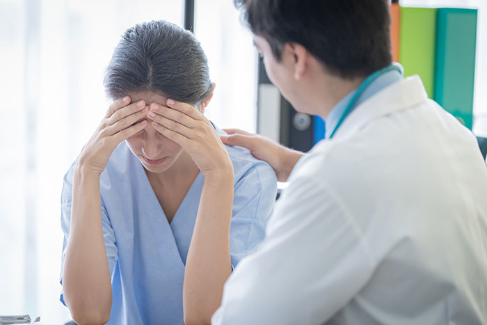 A concerned woman with her head in her hands, being comforted by a doctor about medical symptoms.