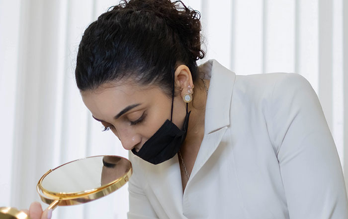 A doctor with a mask looking at a hand mirror, checking for medical symptoms.