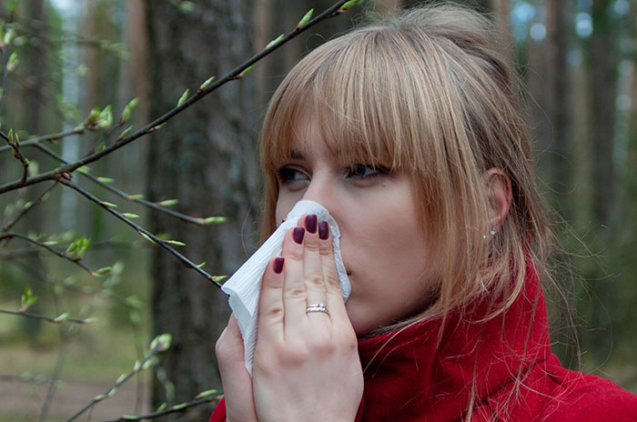 A woman blowing her nose with a tissue outdoors, depicting medical symptoms doctors wish people would stop ignoring.