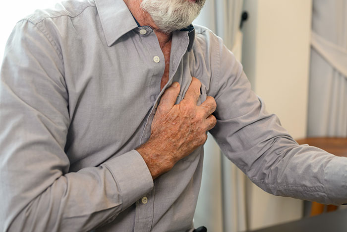 An older man clutching his chest in pain, a medical symptom doctors wish people would not ignore.