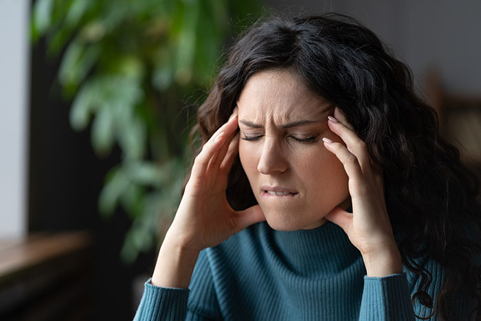 A woman clutching her head, experiencing a headache, a common medical symptom many people ignore.