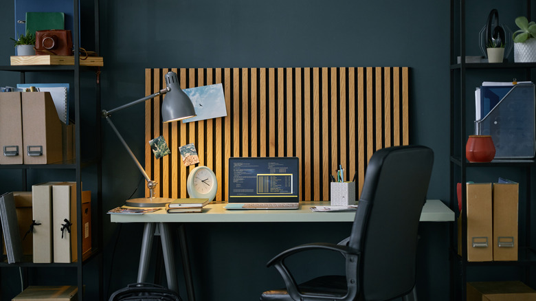 An organized home office with a laptop displaying code on a desk, flanked by shelving units.