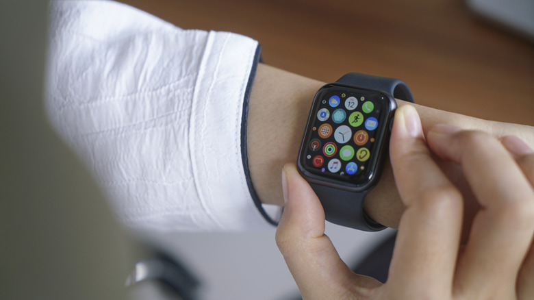 An Apple Watch on a wrist showing icons, two fingers on it, one holding down the Digital Crown.