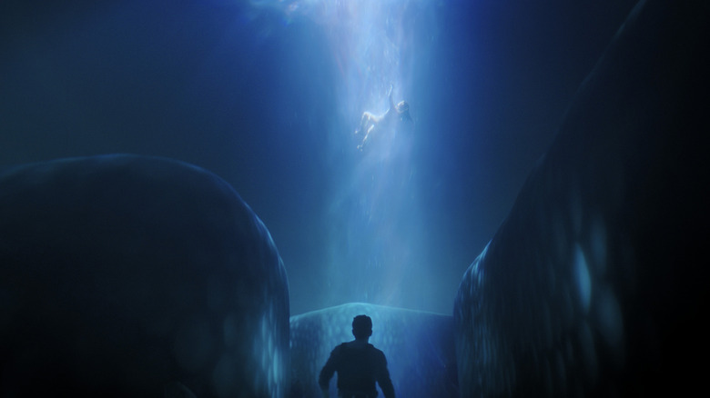 A person with their back to the camera watches on as someone is lifted into the sky by a mysterious beam of blue light.