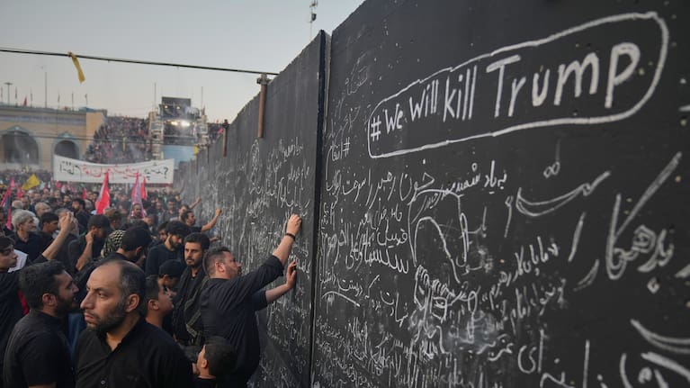 Funeralgoers write messages on a wall, including one saying, "we will kill trump".