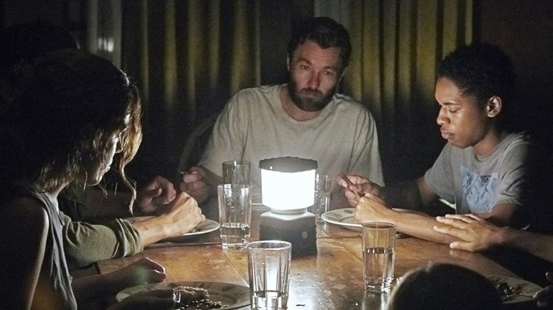 Paul, Sarah, and Kim around a table lit by a lantern in It Comes at Night