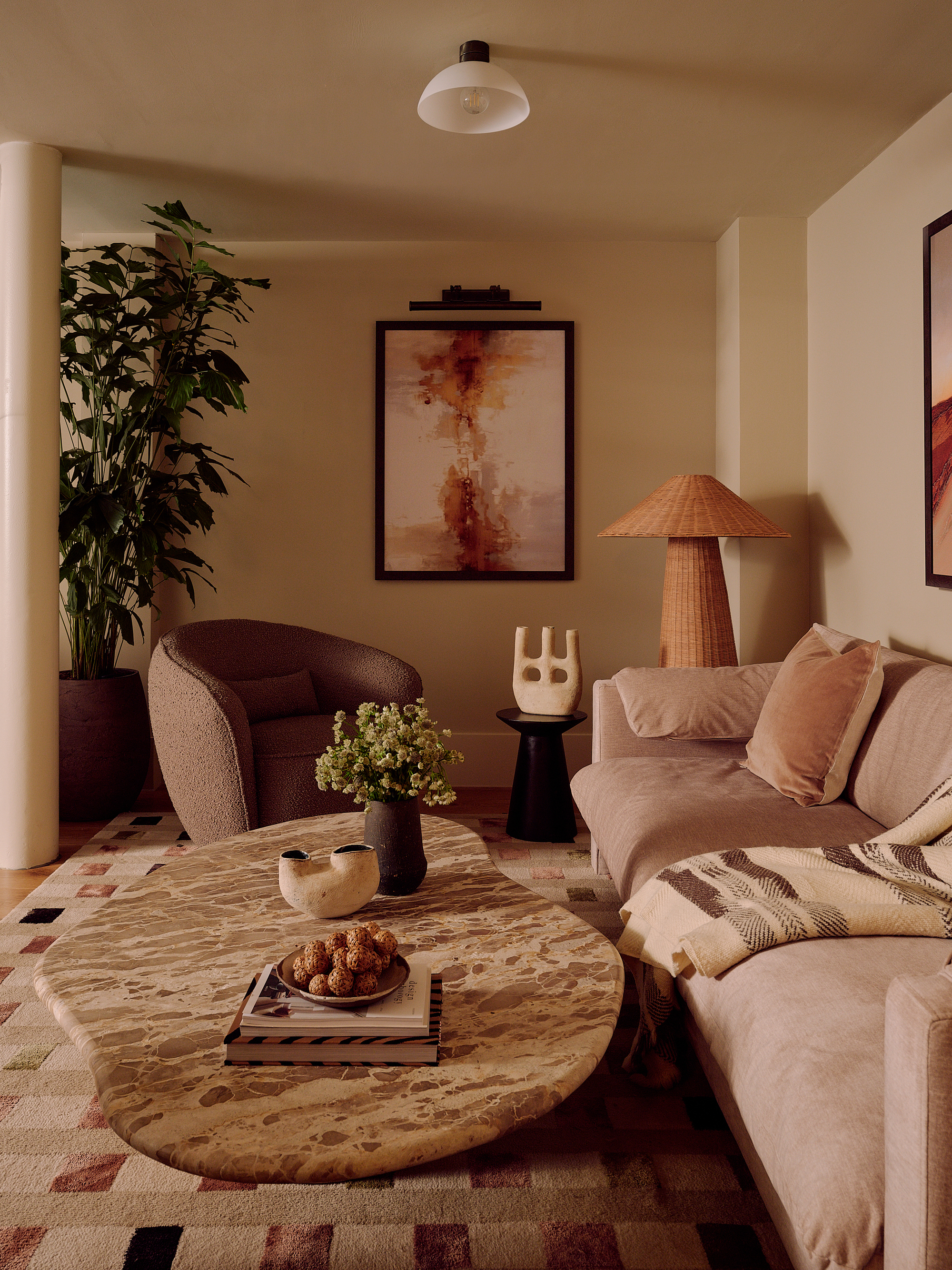 beige living room with marble coffee table, taupe sofa, brown armchair, artwork, with potted plant, rattan armchair, but side table with sculpture