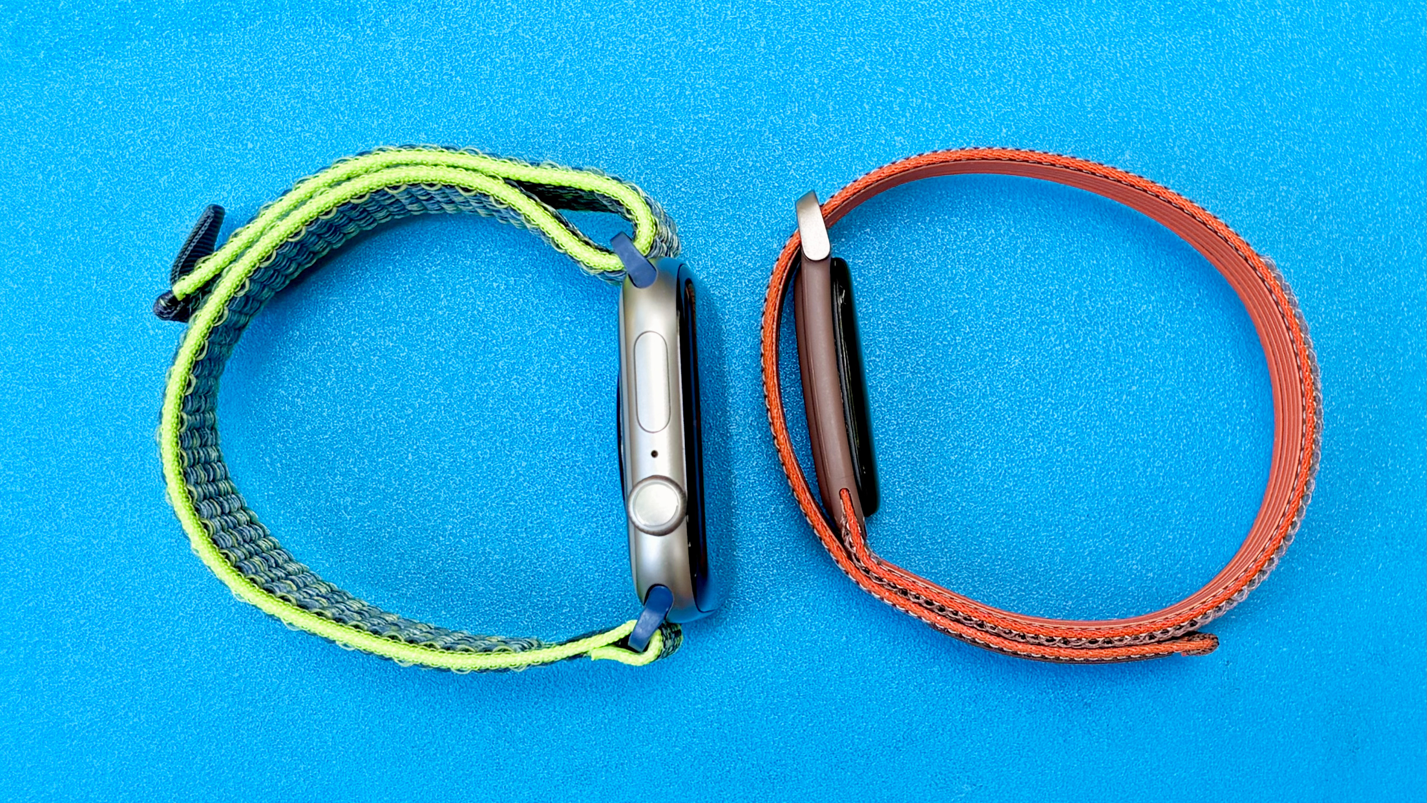 Close-up of the Apple Watch Series 11 next to the Fitbit Air; both are on colorful straps