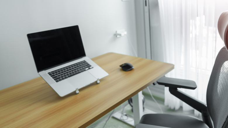 A light-wood home office desk with a laptop elevated on a laptop stand.