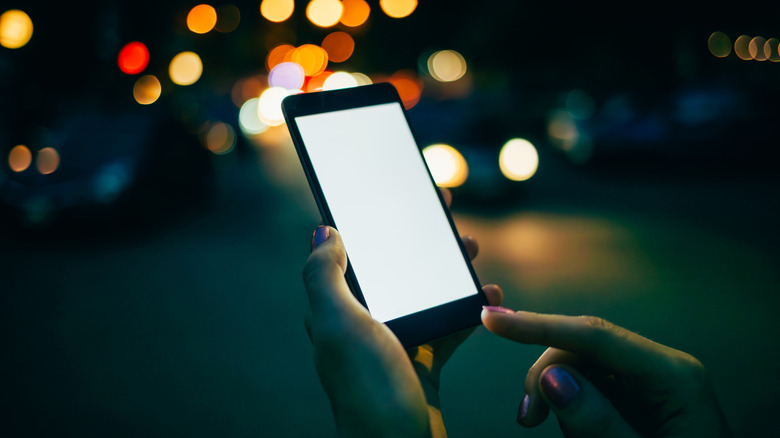 A person holding a phone with a bright screen while outside at night.