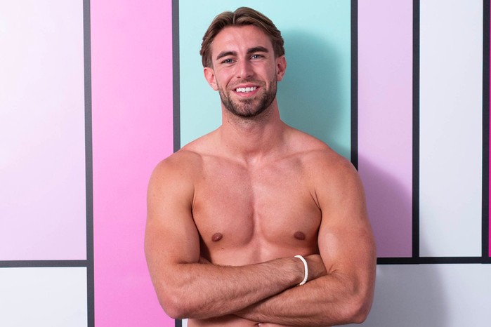 Tommy stands with his arms crossed, smiling and leaning back.