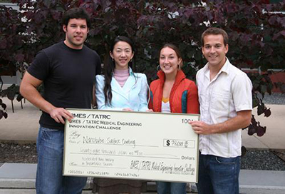 four students stand together holding a large presentation check