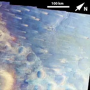 Enhanced-color view of cratered Martian terrain, reddish-brown fading into dusty blue, with pale streaks running across the blue ground.