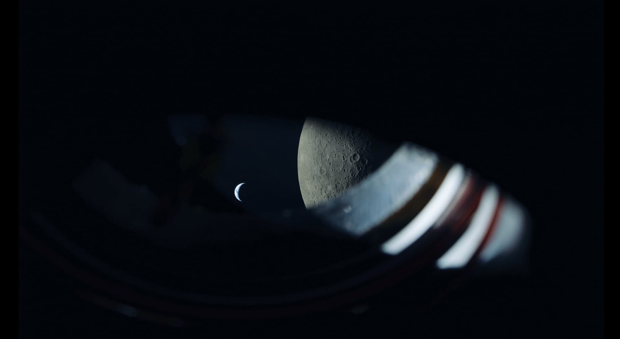 a view from the Artemis II spacecraft showing the edge of the window, the moon, and the earth as a tiny sliver