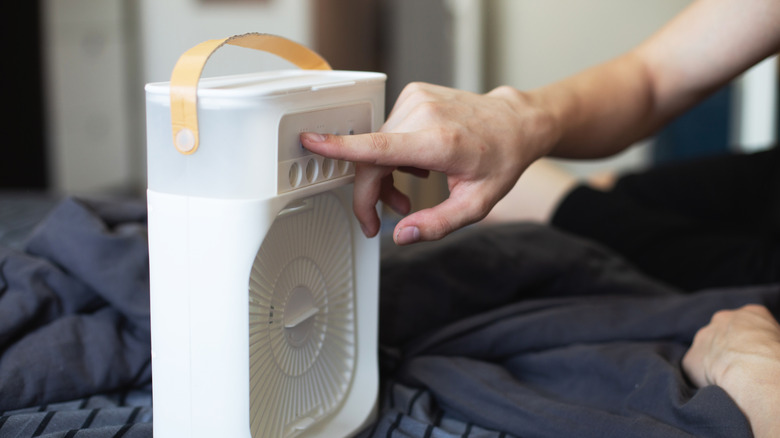 A finger activating a small personal fan or cooler in a bedroom