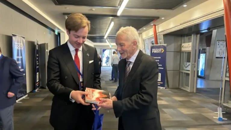Michael Laws signs a book for a supporter at the NZ First party conference in Auckland, July 2026.