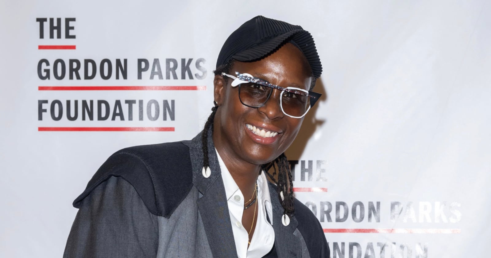A smiling person in glasses and a dark cap poses in front of a backdrop that reads "The Gordon Parks Foundation.
