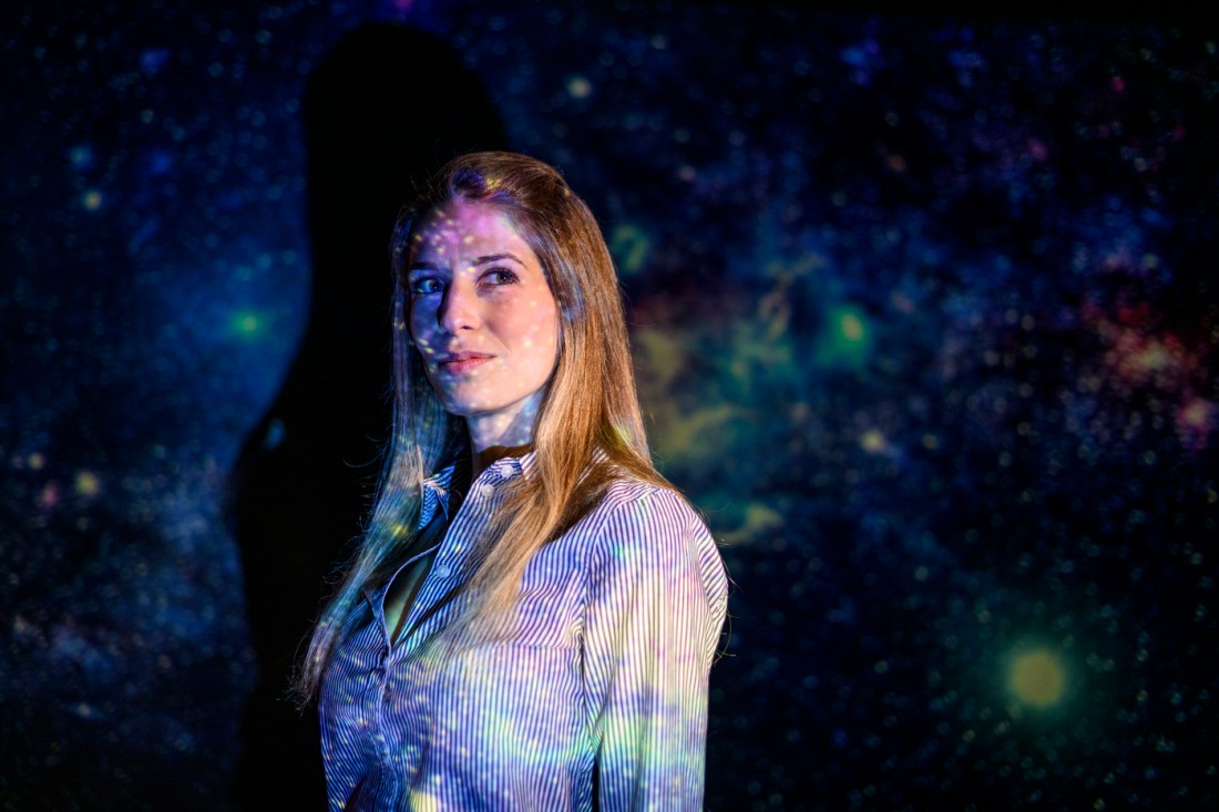 Jacqueline McCleary, associate professor at Northeastern University, standing with a projection of a starfield or galaxy image cast across her face and clothing.